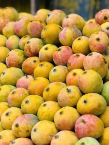 
A vibrant pile of ripe mangoes in various shades of yellow and orange, with some exhibiting hints of pink