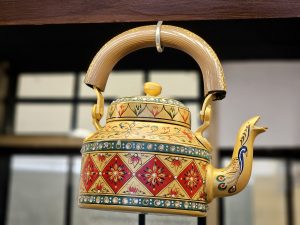 A decorative kettle with colorful patterns and fine artwork displayed indoors at Kurla, Mumbai. The details and design give it a traditional and artistic look. 
