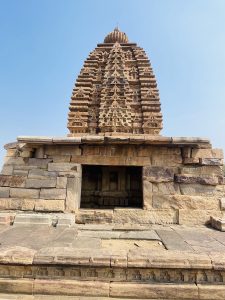 A beautifully carved temple tower rises above a stone base, showing intricate patterns and craftsmanship. Clear sky adds contrast. Taken at Pattadakal, Bagalkot, Karnataka. 
