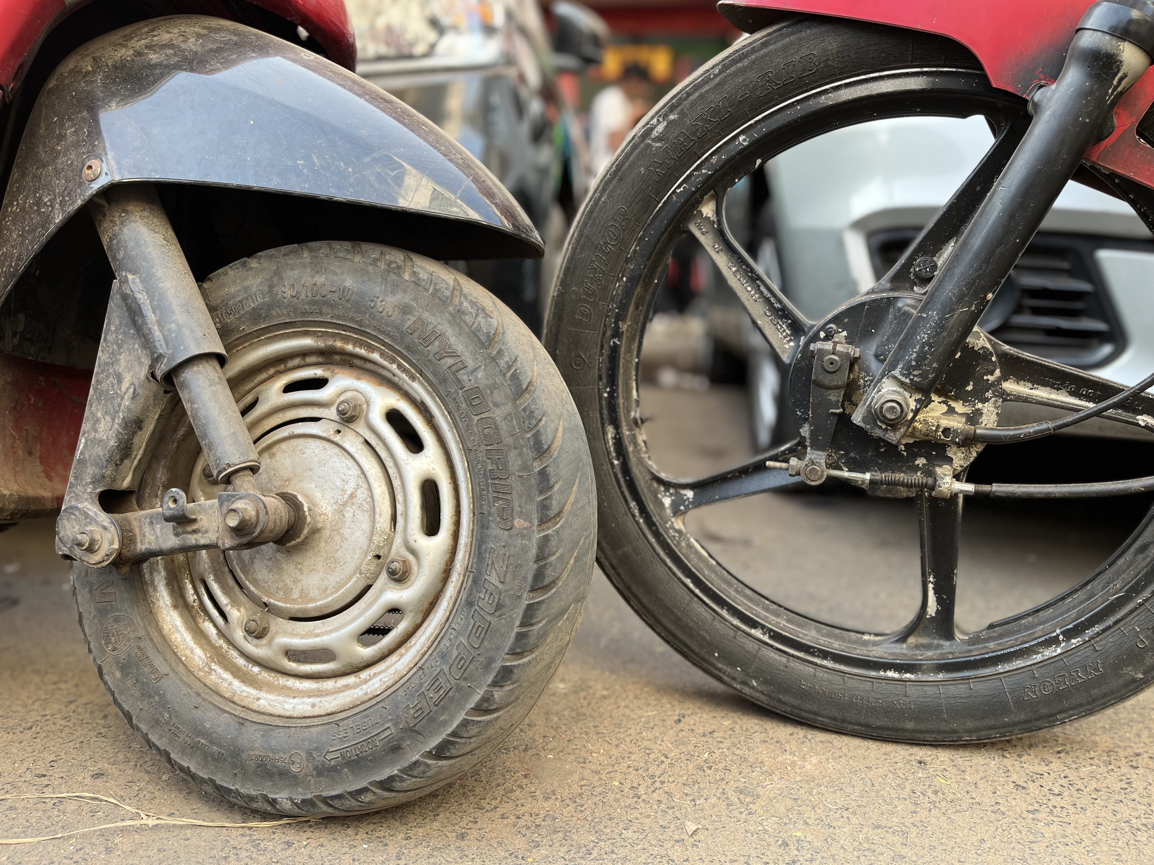 Close-up of scooty and bike wheels side by side on a pavement.