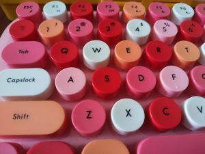 A close-up view of a colorful keyboard featuring round, brightly colored keycaps in shades of pink, red, and white.