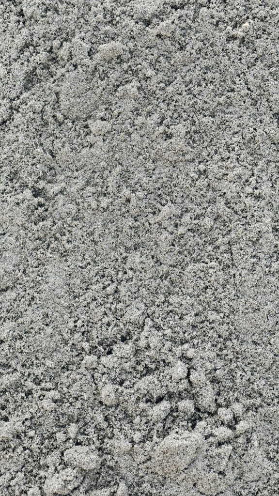A vertical close up shot showing the rough and uneven texture of gray construction sand.