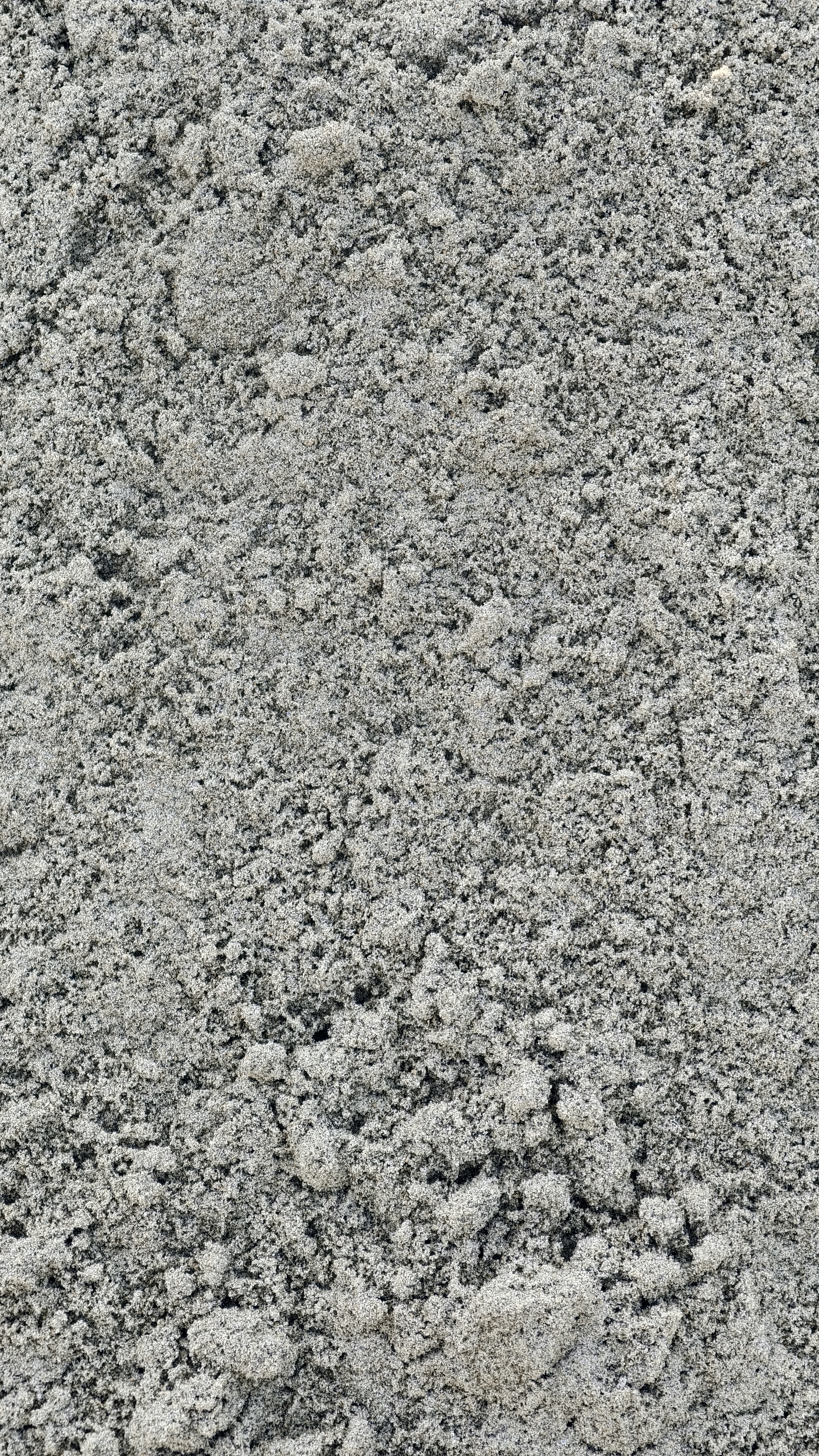 A vertical close up shot showing the rough and uneven texture of gray construction sand.