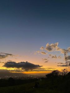 A picturesque sunset view from a hillside, featuring a gradient of colors from deep blue at the top to bright orange and yellow near the horizon. 
