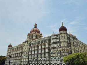 The iconic Taj Mahal Palace Hotel in Colaba, Mumbai, has its grand red dome and detailed architecture. The wide frame and clear sky highlight its beauty and historic charm. 
