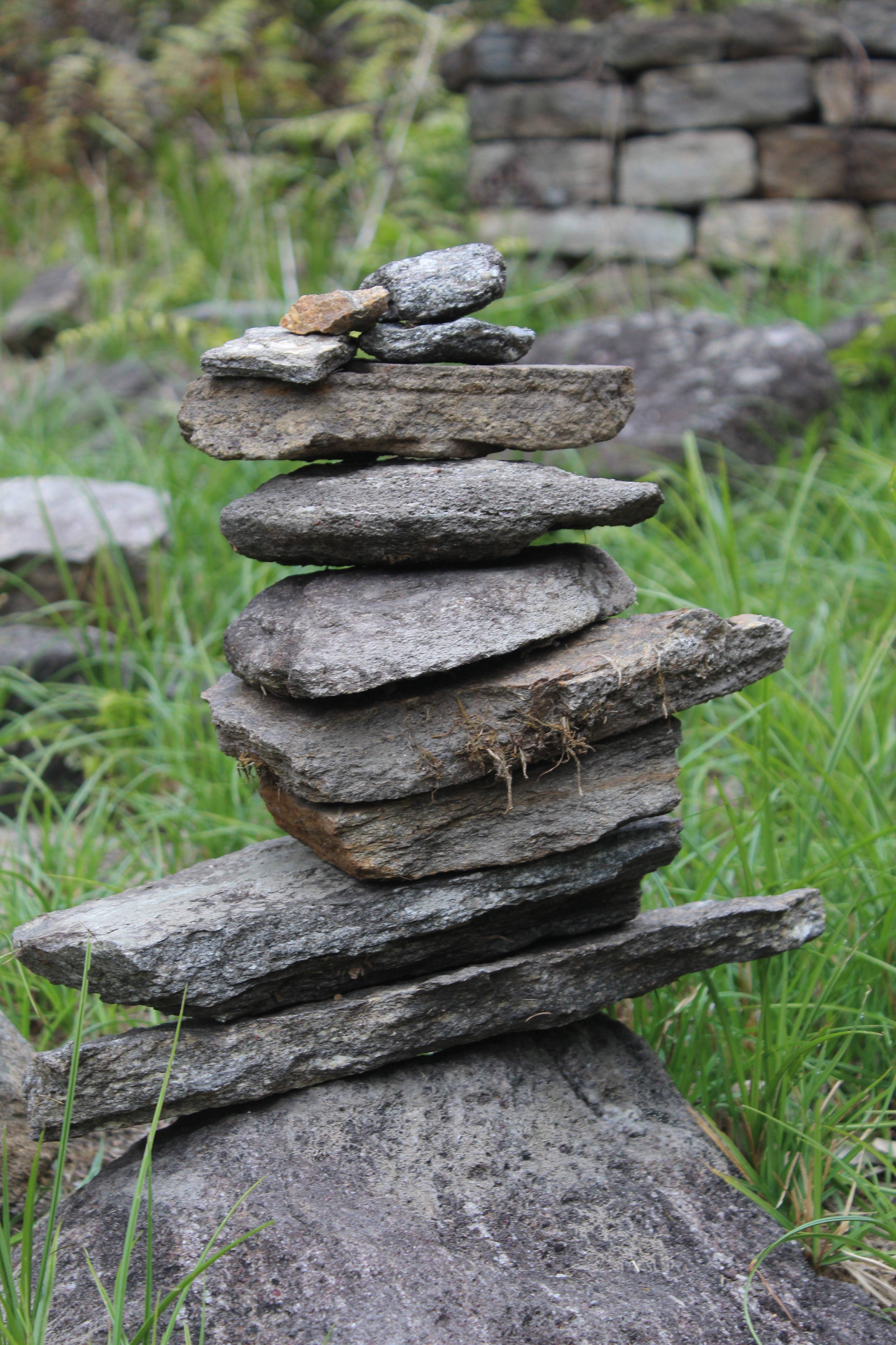 A neatly stacked arrangement of flat stones resting on a larger stone surface, surrounded by green grass.