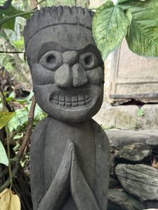 
A carved wooden statue depicting a figure with a stern expression, large eyes, and a broad nose. 