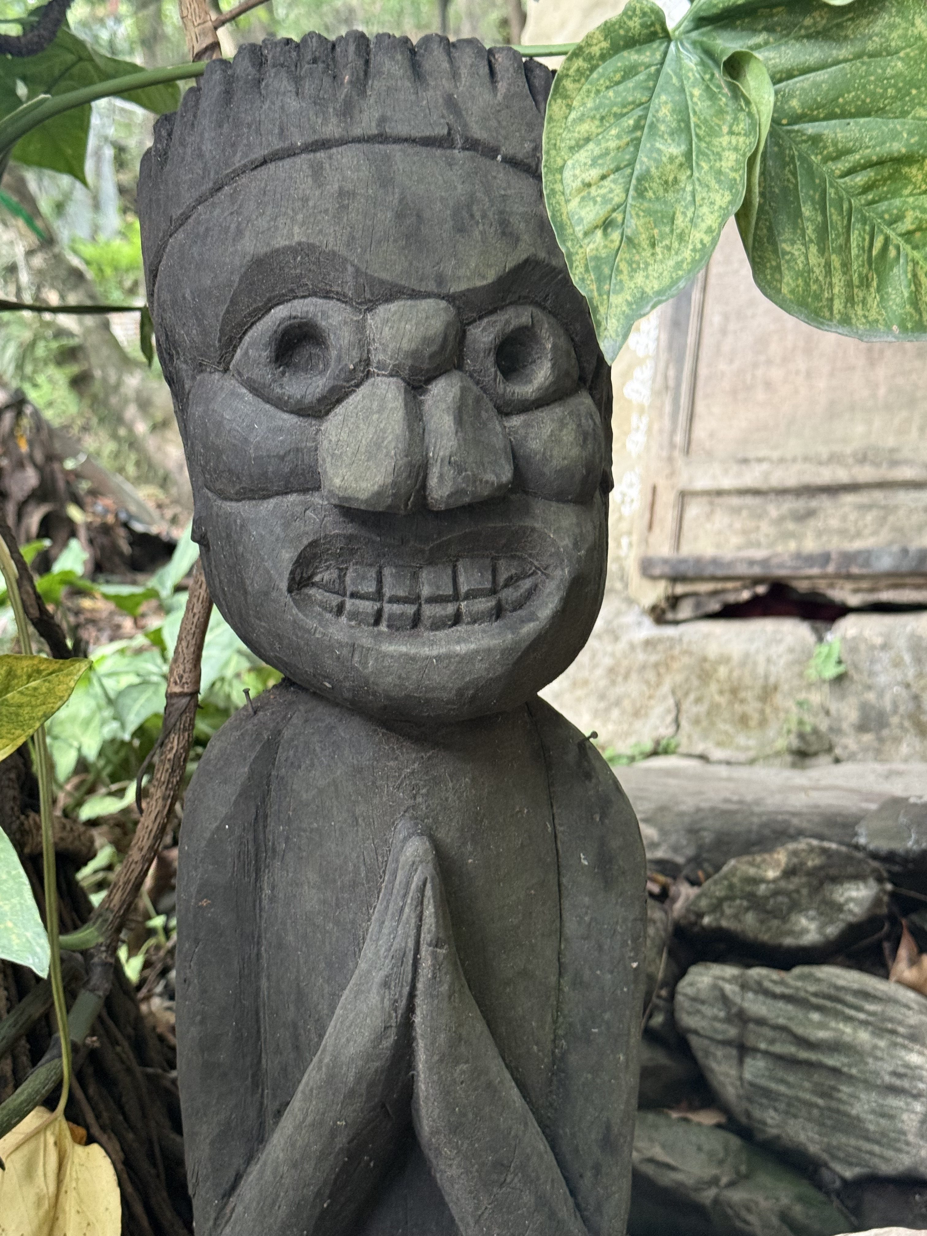 A carved wooden statue depicting a figure with a stern expression, large eyes, and a broad nose.
