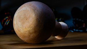 A close-up, side-view photograph of a smooth, hand-crafted wooden object sitting on a wooden surface.