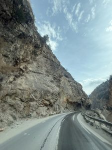 Winding road along a rocky cliff under a partly cloudy sky.
