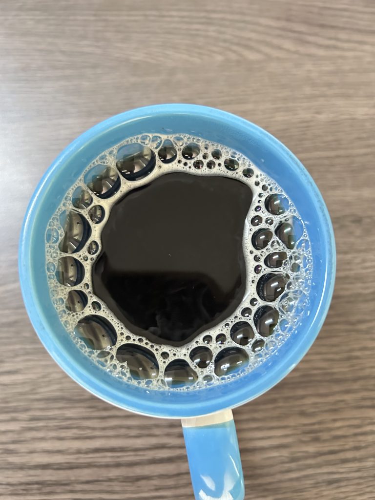A blue cup filled with black coffee, surrounded by bubbles, sits on a table.