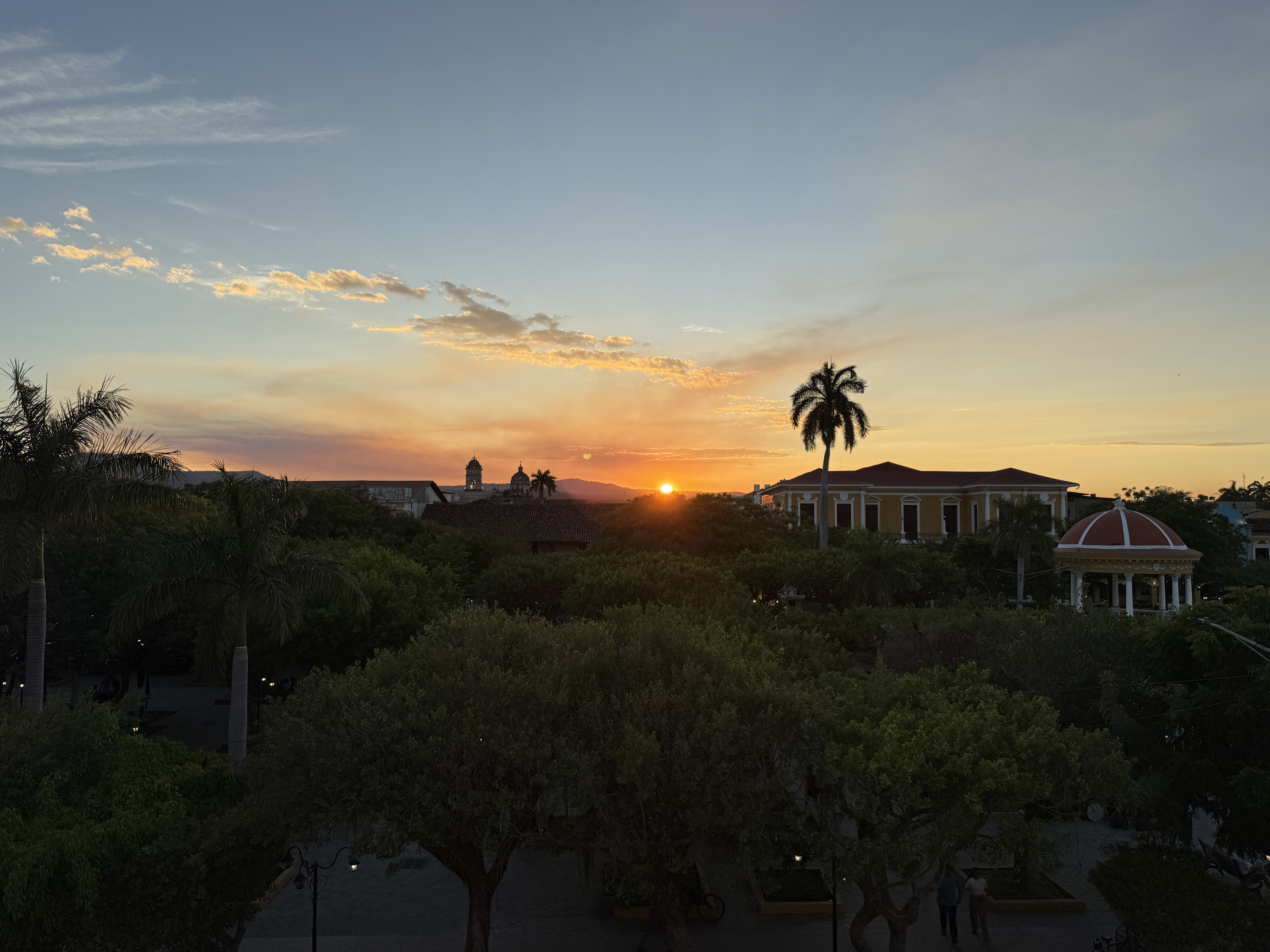Tropical sunset in Granada, Nicaragua, featuring the silhouettes of palm trees against a vibrant orange and pink sky.