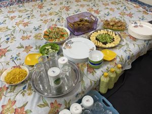 Colorful food spread with salads, fruits, pastries, and drinks on a floral tablecloth.