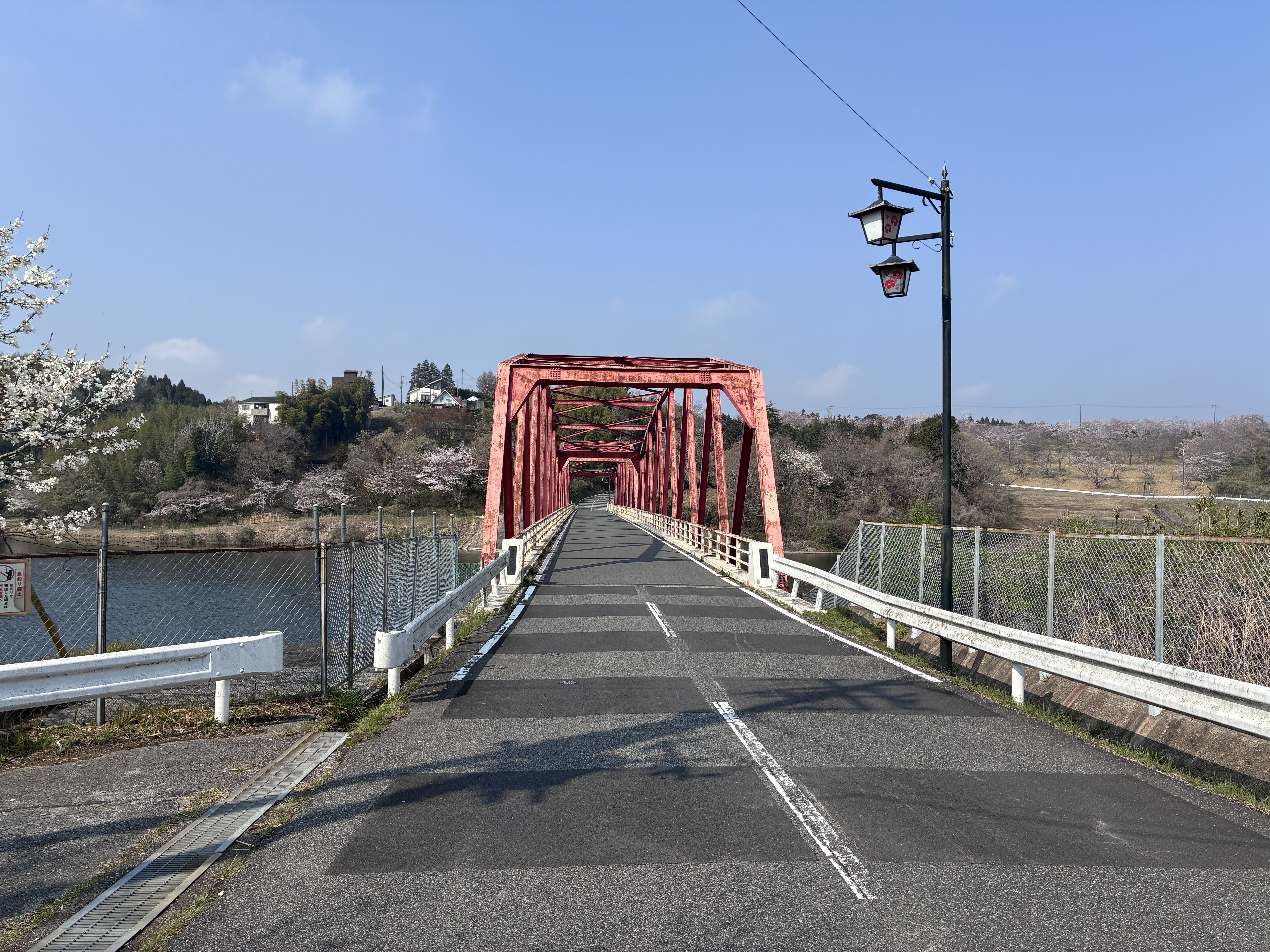 A red bridge spans over a calm body of water, with a blue sky overhead and scattered clouds