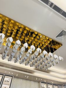 Hanging art installation with white geometric shapes suspended from the ceiling. A golden reflective panel enhances the elegant and modern ambiance.