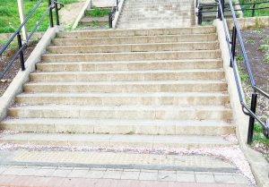 A set of concrete stairs leads upward, flanked by black railings.
