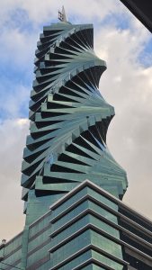 

A modern, spiral-shaped building with a glossy glass facade, twisting in a dynamic form against a backdrop of partially cloudy skies. 