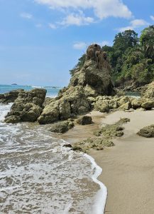 
A rocky beach scene featuring a cluster of large, weathered rocks emerging from the sandy shore
