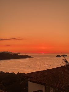 Sunset over calm ocean at Hermosa Beach, Costa Rica, with orange sky, silhouettes, and boats.