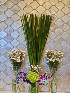 A neat floral arrangement with green leaves and white flowers placed in glass vases against a patterned wall. A calm and balanced decor scene in Bandra Kurla Complex, Mumbai.