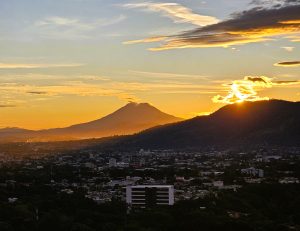 A warm sunset over a city landscape with a mountain silhouette in the background, highlighting the contrast between urban and natural scenery.