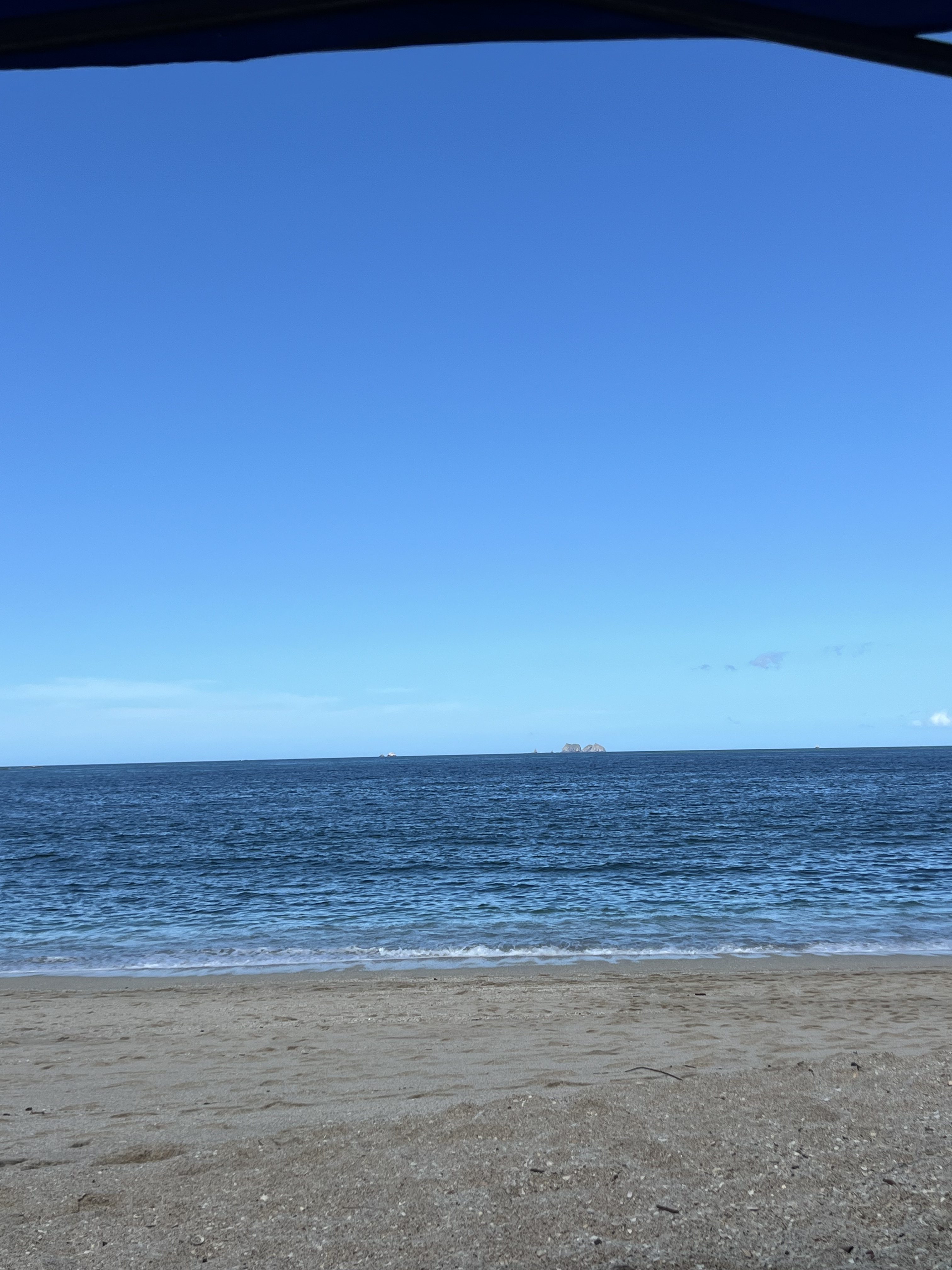 A quiet beach with gentle waves, clear blue water, and a wide open sky stretching across the horizon.