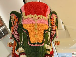 
A large floral sculpture of an elephant adorned with vibrant colors, featuring elaborate decorations made of flowers in red, pink, orange, and green.
