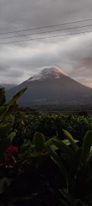 A volcano capped with clouds and surrounded by lush vegetation, creating a dramatic and peaceful landscape.