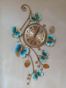 Gold wall clock with black numerals, surrounded by metal branches adorned with blue and gold butterflies and decorative leaves.