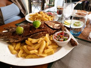 Grilled whole fish with crispy fries, lime halves, and a side of fresh salsa on a white platter.