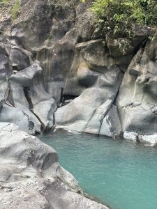 A secluded section of a river canyon with sculpted grey rocks surrounding bright turquoise water and green vegetation at the top.