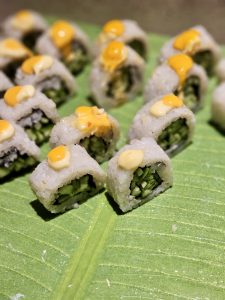 Small sushi rolls topped with creamy sauce, placed on a green leaf. A neat and minimal food composition captured in Worli, Mumbai.