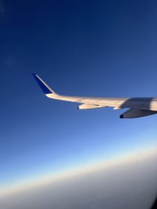 A view from an airplane window featuring a wing extending out into the clear blue sky.