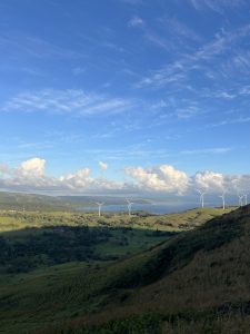 Panoramic view from Tilarán viewpoint overlooking Lake Arenal, with green hills and wind turbines in the foreground.
