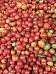 A colorful assortment of small tomatoes in various shades of red, orange, and a few green ones, densely packed together in a vibrant display.