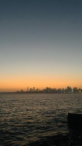 Marine Drive at night in Mumbai, with glowing streetlights along the curved coast reflecting on the Arabian Sea and city lights in the background.
