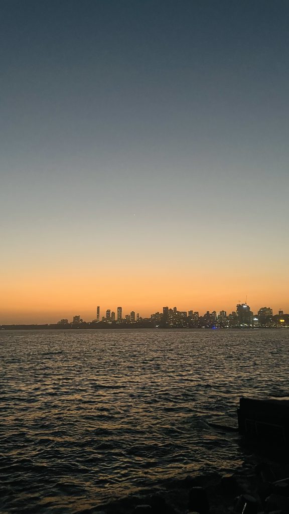 Marine Drive at night in Mumbai, with glowing streetlights along the curved coast reflecting on the Arabian Sea and city lights in the background.