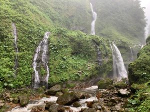 
A scenic view of lush green mountains adorned with multiple waterfalls cascading down rocky cliffs