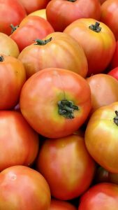 
A pile of ripe, round tomatoes with a smooth surface, showcasing a gradient of orange to red colors.