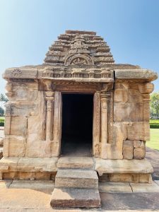 A small stone shrine with a simple entrance and carved pillars. The aged texture and warm tones reflect history. Shot at Pattadakal, Bagalkot, Karnataka.
