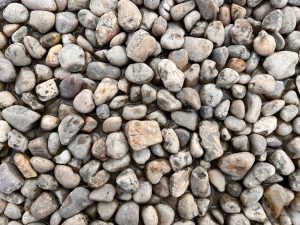 A collection of smooth, rounded pebbles in various shades of gray and brown, some wet, creating a natural, textured surface