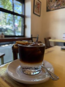 A glass of cold brew coffee with ice cubes and two lemon slices on the rim, served on a small white plate.