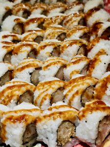 Rows of sushi rolls are topped with a glossy sauce, creating a rich, tempting appearance. A detailed food shot captured in Worli, Mumbai. 