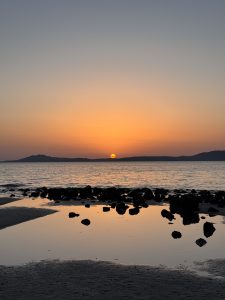 A serene sunset over the sea at Sardinia, with the glowing orange sun dipping below the horizon.