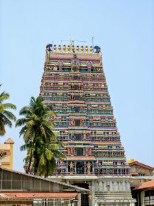 Colorful gopuram of the Sharada Temple rises in intricate Dravidian tiers, framed by coconut palms under a clear blue sky.
