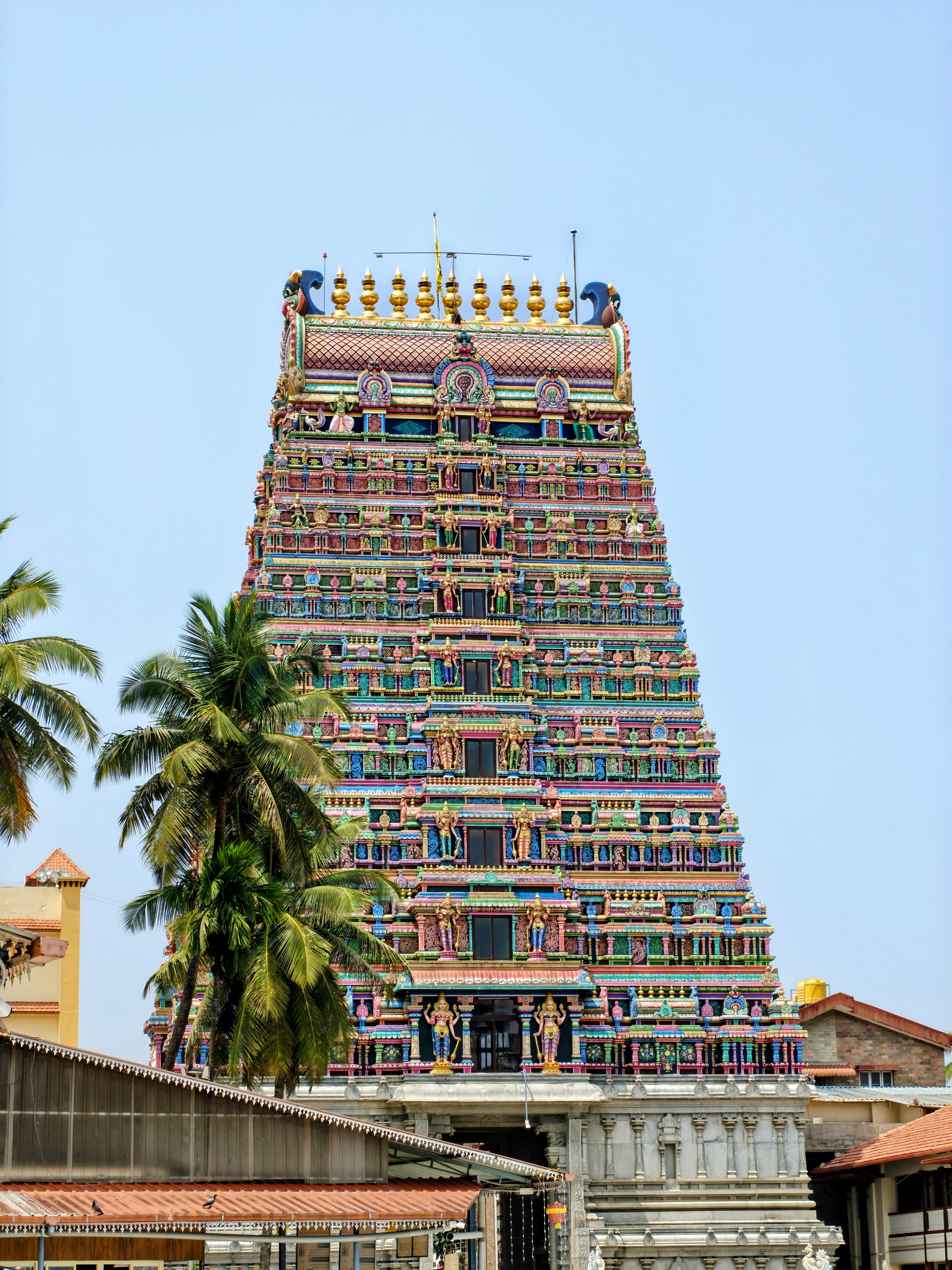 Colorful gopuram of the Sharada Temple rises in intricate Dravidian tiers, framed by coconut palms under a clear blue sky.