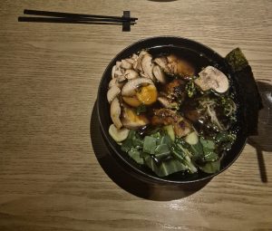 Asian soup with vegetables, chicken, mushrooms, egg, and seaweed, with chopsticks at the top.