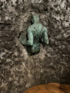 Bronze sculpture of a human figure crouching against a stone wall, part of the Cave Tour in Costa Rica