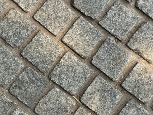 A close-up view of a cobblestone pavement, featuring square granite stones arranged in a diagonal pattern.