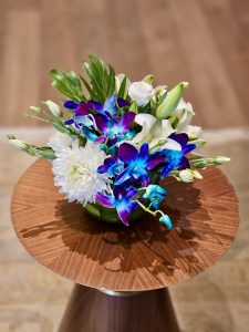A colorful bouquet of fresh flowers is placed on a round wooden table, with a soft, blurred background. A simple and elegant decor shot in Bandra Kurla Complex, Mumbai.